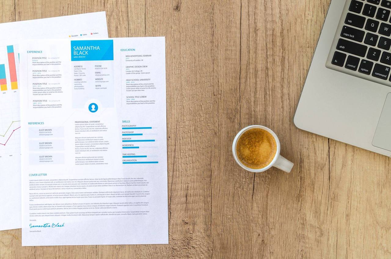 A printed resume beside a laptop and a cup of coffee